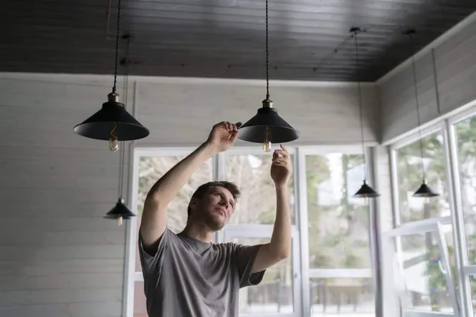 Man Is Captured Act Changing Light Bulb Hanging Ceiling Light Fixture With Natural Daylight Illuminating Scene 1 X - Certified Lighting Consultant study guide