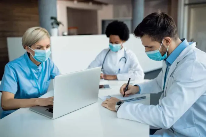 Male Doctor Taking Notes While Working With Colleagues Medical Clinic X - Certified Public Health Administrator study guide