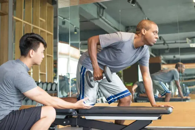 Trainer Helping Man Lifting Dumbbell Gym - Certified Strength &amp; Conditioning Specialist study guide